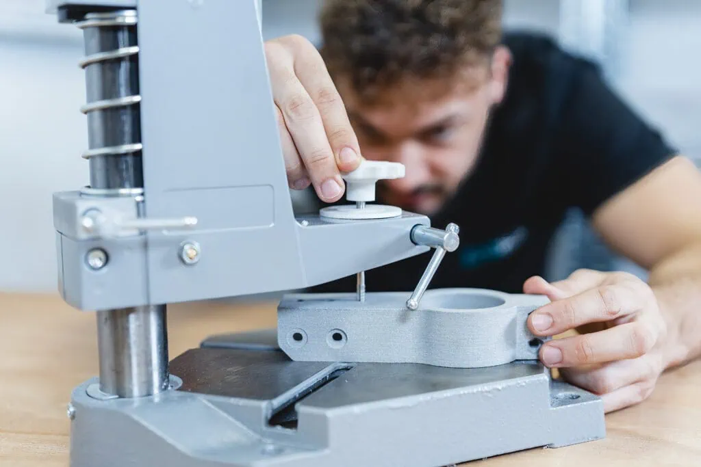 Ein Mitarbeiter von prioadd schneidet mithilfe einer Vorrichtung ein Gewinde in ein SLS-Bauteil aus dem Werkstoff Alumide.