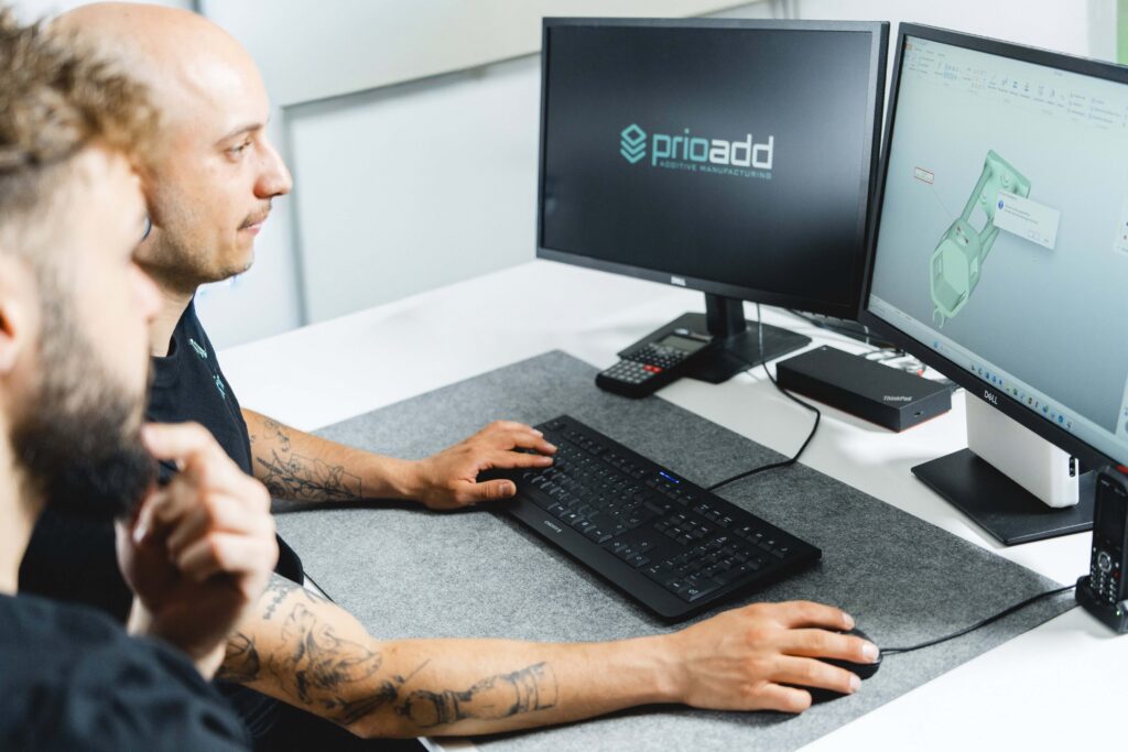 Zwei prioadd-Mitarbeiter konstruieren am PC ein SLS 3D-Druck Bauteil im CAD.
