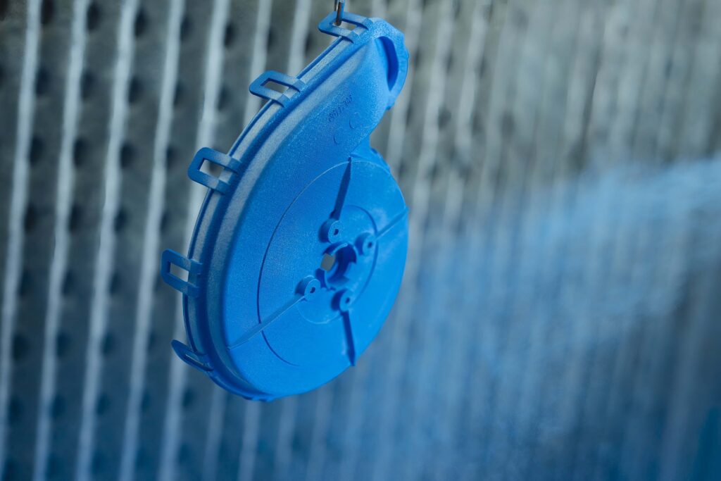 An SLS 3D-printed component is coated with blue paint in a coating booth.