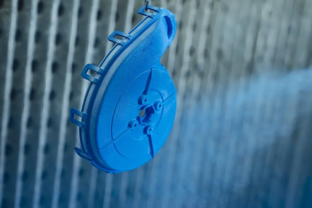 An SLS 3D-printed component is coated with blue paint in a coating booth.