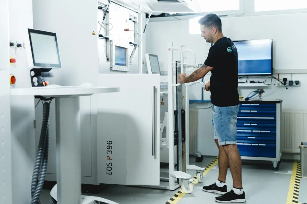 An employee of prioadd is preparing an SLS 3D printer for the next machine run.