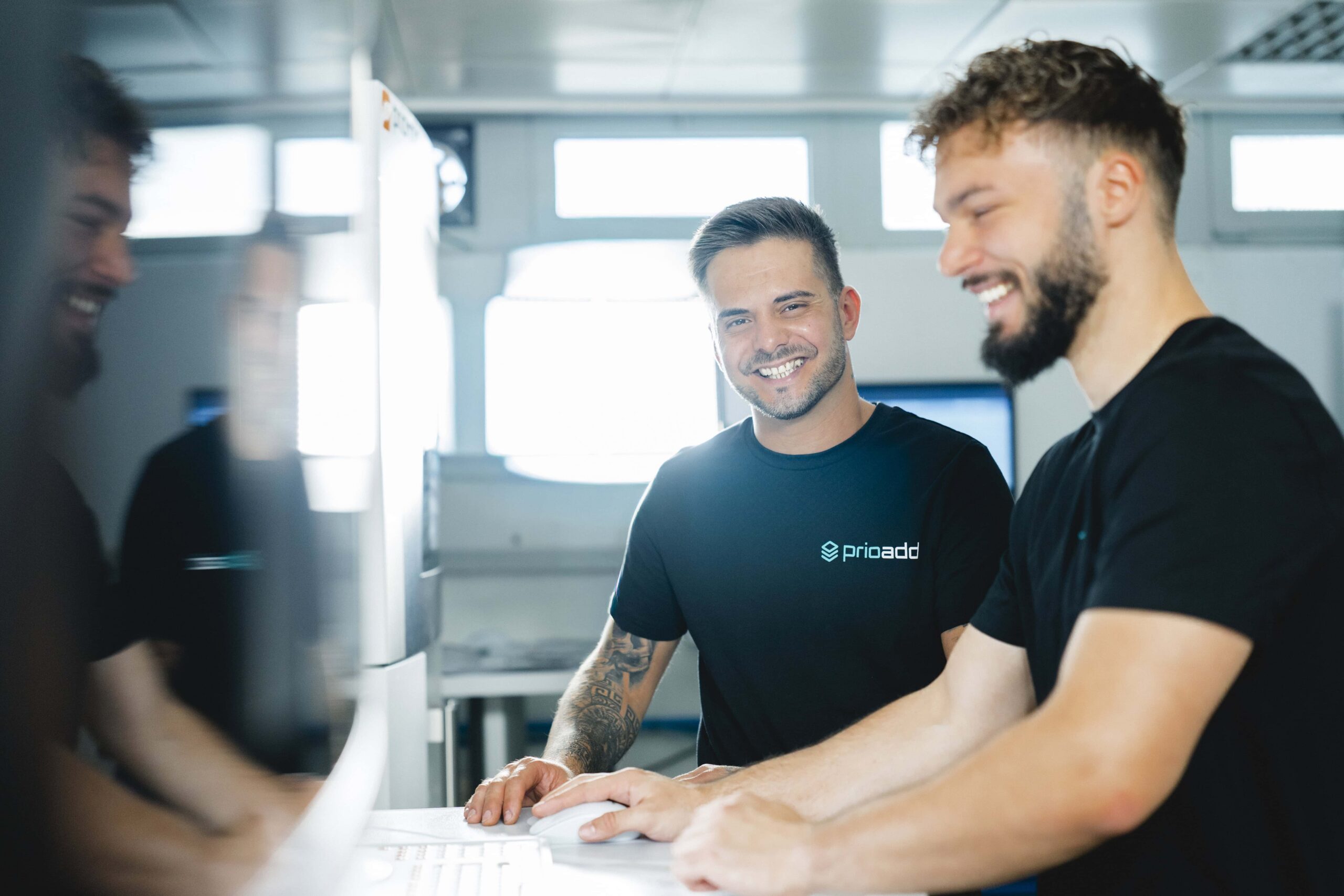 Deux employés de prioadd se tiennent devant une machine d’impression 3D SLS.